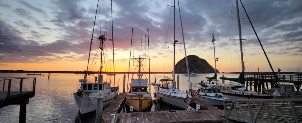 Morro Rock at sunset with boats along a dock.